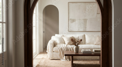 A serene living room with a white linen sofa, a wooden coffee table with books and a vase of dried flowers, and a large abstract painting on the wall.