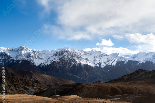 Spectacular mountain range with snow-covered peaks under a bright blue sky in Ladakh, India. High altitude desert landscape with rocky terrain and winter scenery. Panoramic view of Himalayan nature.