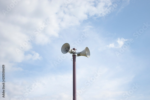 Foto Outdoor public address speakers on pole against blue sky with clouds