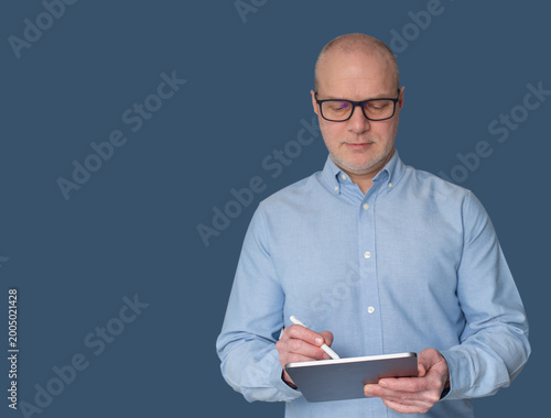 Professional businessman in light blue shirt and glasses holding a tablet and stylus against dark background. Concept of leadership, technology, and innovation.