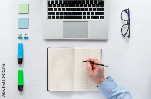 Top view of a laptop, open notebook, and hand writing with a pen. Symbol of creativity, planning, and productivity in a modern workspace.