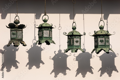 Tableau sur toile Row of traditional bronze hanging lanterns with green patina casting dark shadow