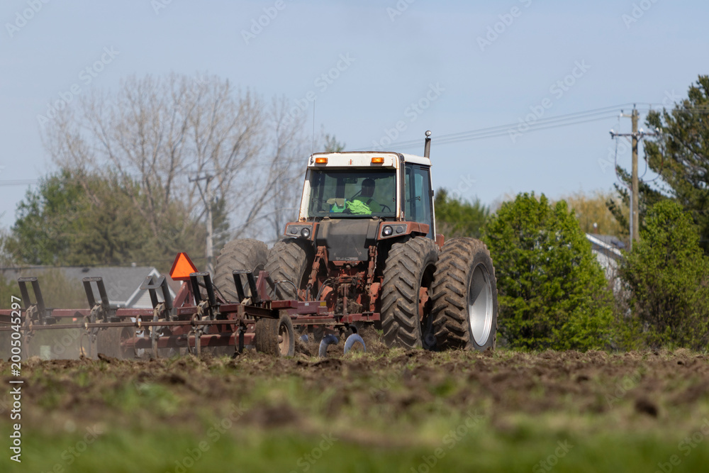 Obraz premium A farmer man in a bright green shirt driving a tractor machine on a farm field.