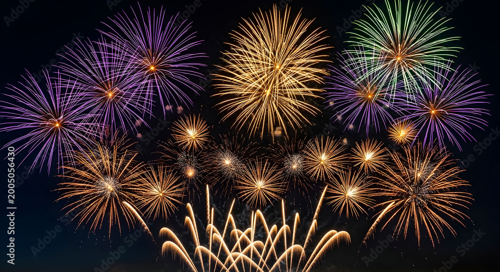 Fototapeta premium Dazzling fireworks illuminate night sky with vibrant explosions of purple gold and green light over dark landscape offering celebratory holiday festive atmosphere.