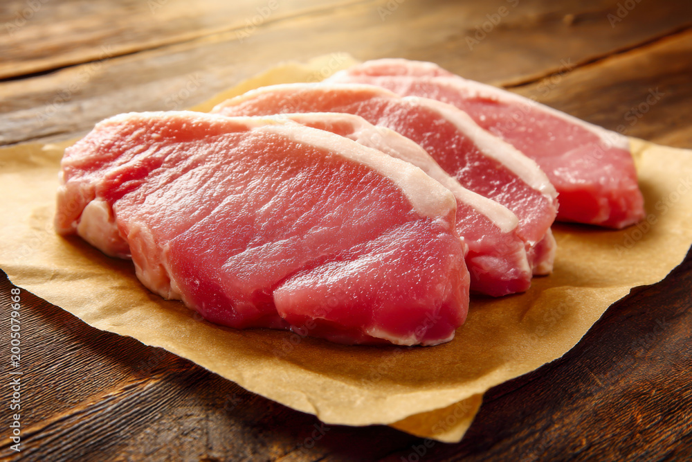 Fototapeta premium Fresh raw pork loin steaks on brown parchment paper over a rustic wooden background