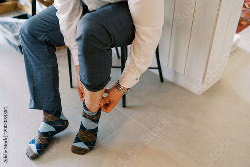 Obraz na płótnie Gentleman seated adjusting vibrant patterned socks prior to gathering