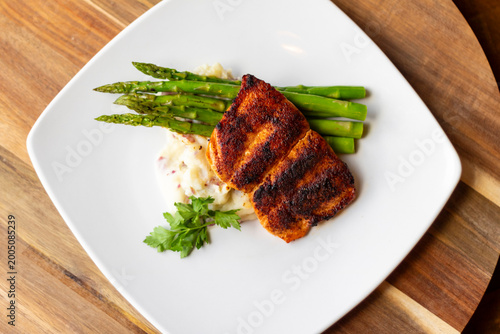 Obraz na plátne Grilled salmon meat, asparagus and mashed potatoes on a white plate sitting on a wooden table in a restaurant