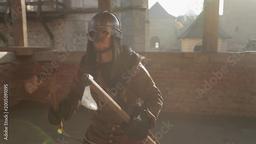 Male medieval warrior swinging battle axes in both hands inside fortress courtyard with dramatic golden backlight and cinematic lens flare. Powerful action reenactment footage for history and fantasy 