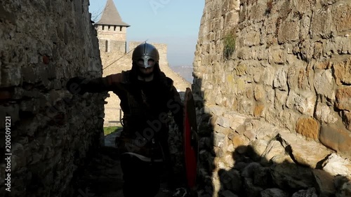 Viking warrior in full armor running through narrow stone castle passage and drawing sword for battle. Dynamic high-energy cinematic action shot for historical reenactment and fantasy content.