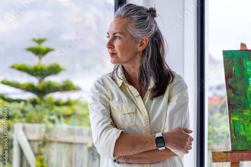 Foto Senior woman standing with smartwatch and arms crossed by easel with green canva