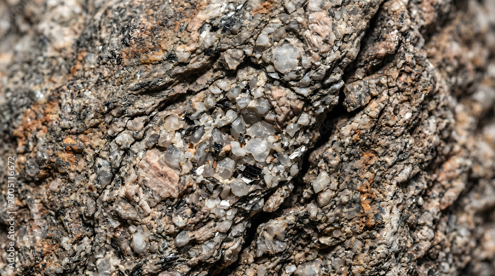 Fototapeta premium Close-up texture of a rough, weathered granite rock reveals a complex interplay of mineral grains in earthy tones and subtle cracks.