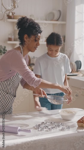 African american mother and her teen daughter cooking together at home kitchen. Happy motherhood and childhood, mom and child sifting flour on table, baking pie or cookies for dessert and dinner