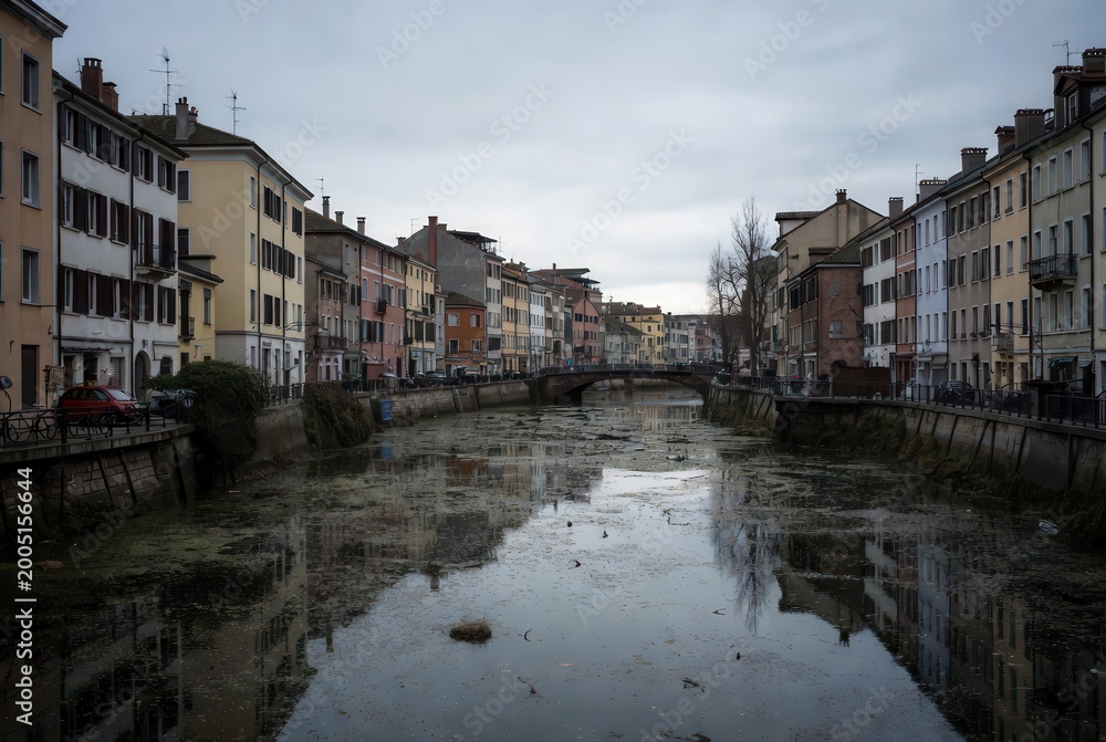 Obraz premium European canal lined with colorful buildings and reflections on a cloudy day