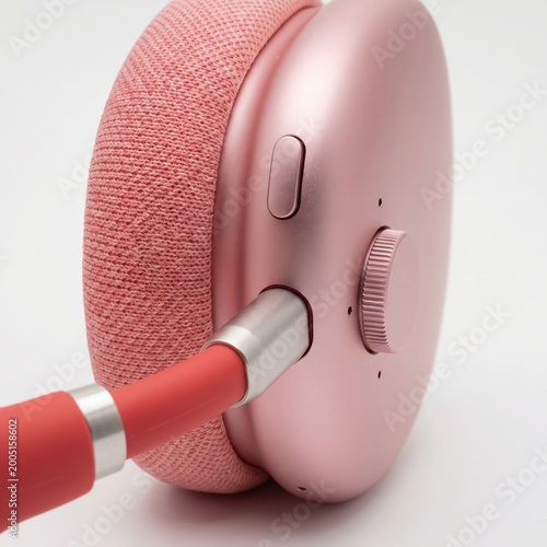 Pink wireless headphones detail with audio cable and volume control dial close up view.
