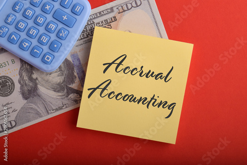 Accrual accounting concept with calculator, dollar banknote, and sticky note on red background, representing financial reporting, bookkeeping, business finance, and accounting principles.