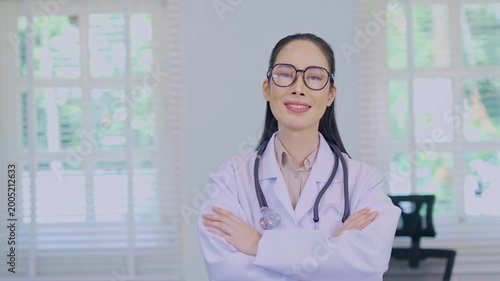  A portrait photograph of a smiling female doctor in a white lab coat, looking at the camera, standing in a hospital setting with her arms crossed.