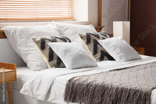 Fotografie Cozy bed with soft pillows near window in light bedroom