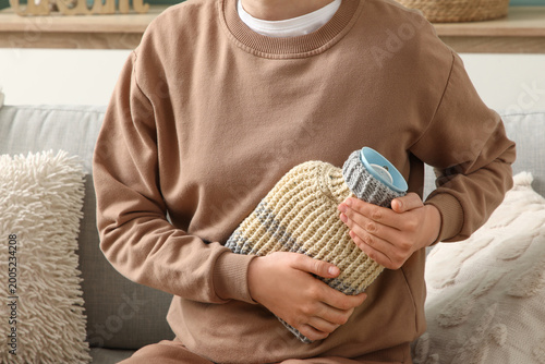 Obraz na płótnie Woman warming her belly with hot water bottle on sofa at home
