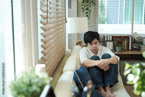 Φωτογραφία Young asian man sitting on couch feeling overwhelmed and stressed
