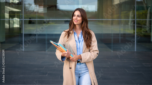 Canvas-taulu Businesswoman looking ahead holding folders in front of modern building