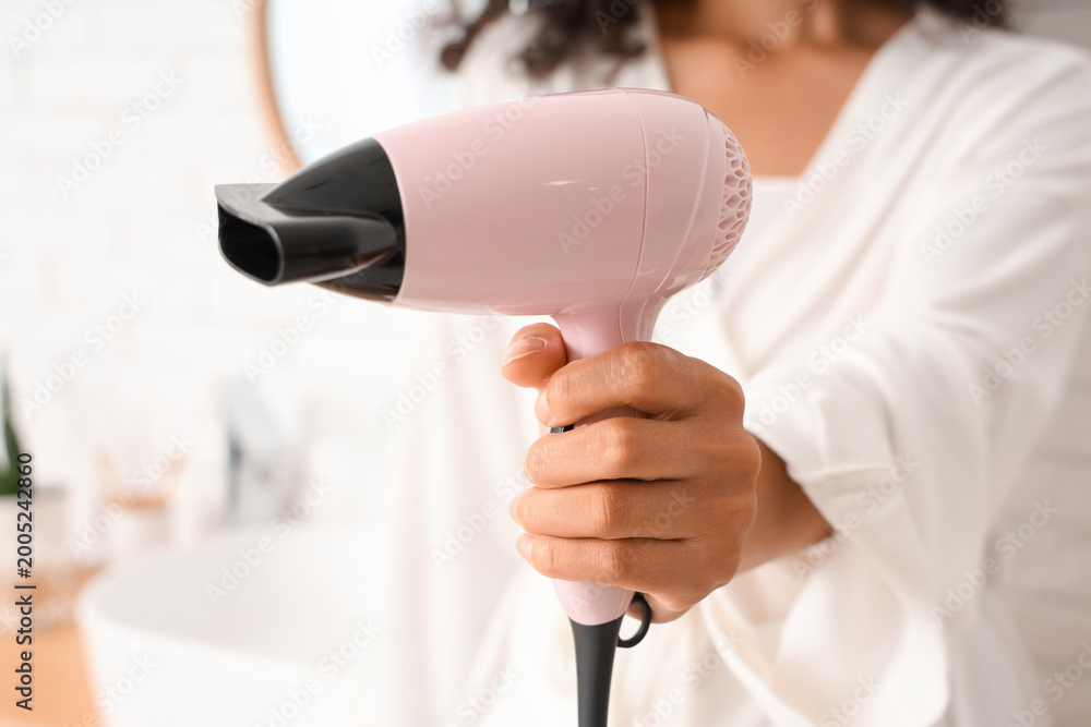 Fototapeta premium Young African-American woman with modern hair dryer in bathroom, closeup