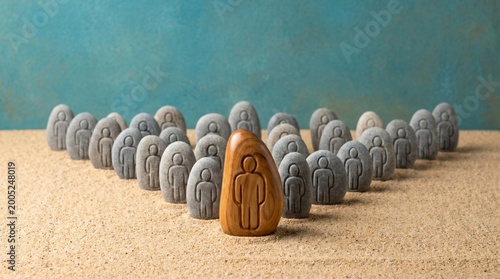 Wooden Figure Leading Group of Stone People Carvings Representing Leadership and Individuality on Sand Background