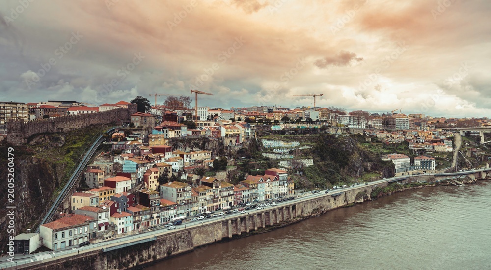 Obraz premium A scenic view of Porto's historic hillside neighborhood reveals colorful buildings along the river. Construction cranes dot the skyline, highlighting urban transformation amidst tourist crowds