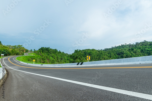 Long curvy forest asphalt road over the hills. Beautiful curved road in the forest. Side view of road.
