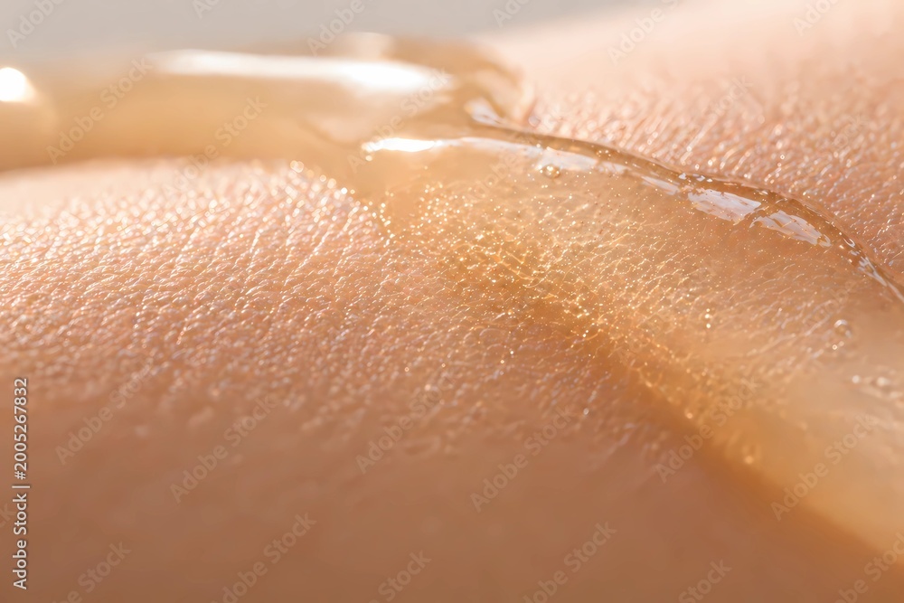Fototapeta premium Detail of a soothing liquid drop on hand, concept of wellness and organic beauty.