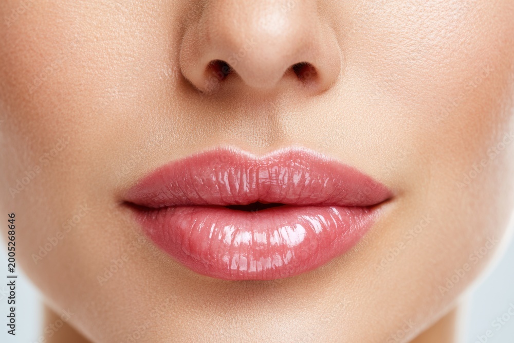 Naklejka premium Close-up of female lips with natural texture and glossy finish, showcasing soft pink color and smooth contours against a neutral background