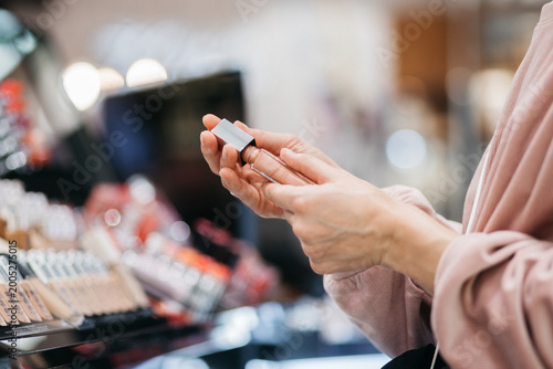 Foto Female standing in makeup section choosing lipstick in retail store