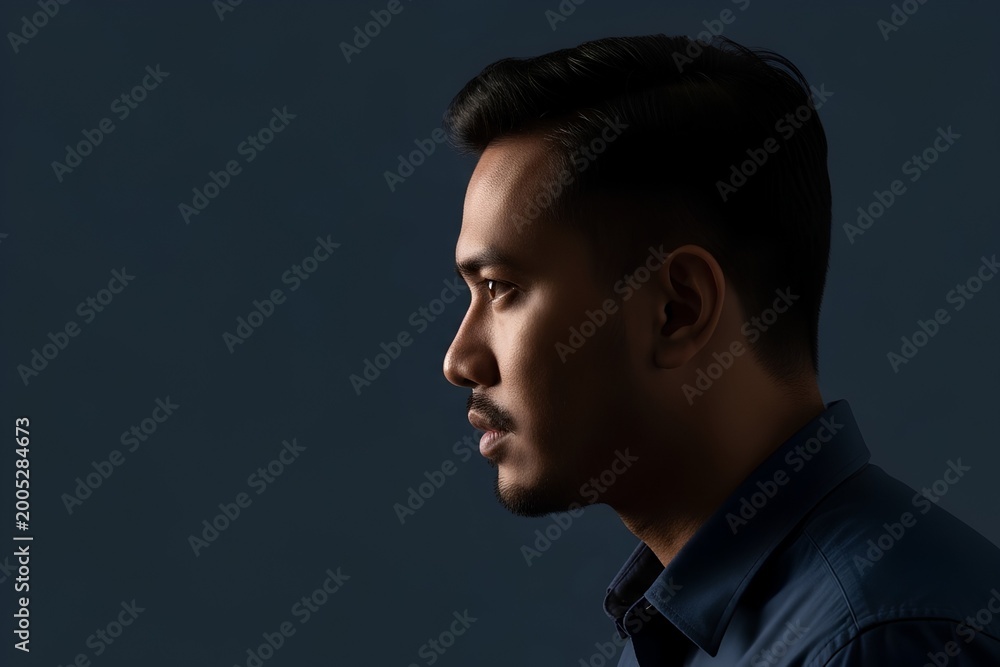 Fototapeta premium Young Asian Man Profile Portrait Dark Background Blue Shirt Cinematic Photography Copy Space Isolated
