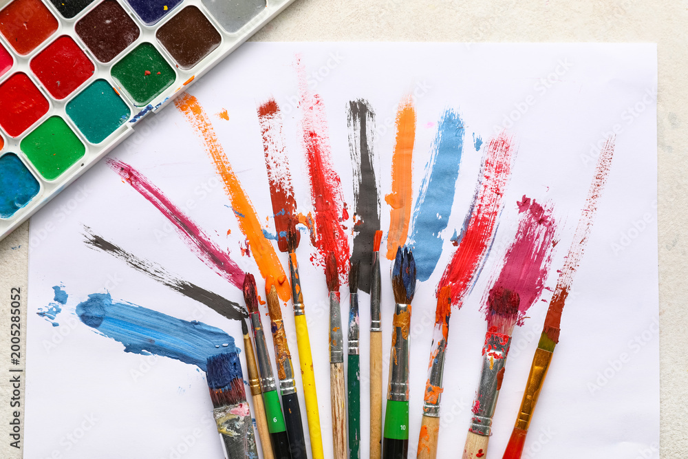 Obraz premium Artist brushes with paint strokes and sheet of paper on white grunge background