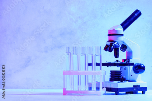 Holder with test tubes and modern microscope on blue background