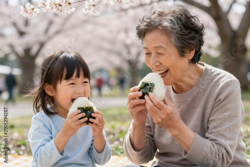 Japanese grandmother and granddaughter laughing eating onigiri during picnic