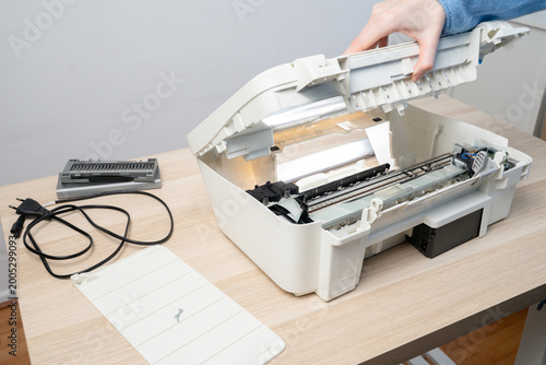 Bild auf Leinwand Person performing maintenance on an open white inkjet printer scanner on desk, showing internal components, power cable and removed parts, illustrating repair, troubleshooting and office technology