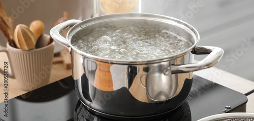 Fotografie Stainless steel pot with boiling water on stove in kitchen, closeup