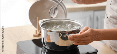 Woman and stainless steel pot with boiling water on stove in kitchen, closeup