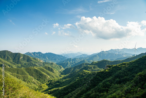 Wind turbines on green mountain ridges in rural China, representing renewable energy development and sustainable power generation.