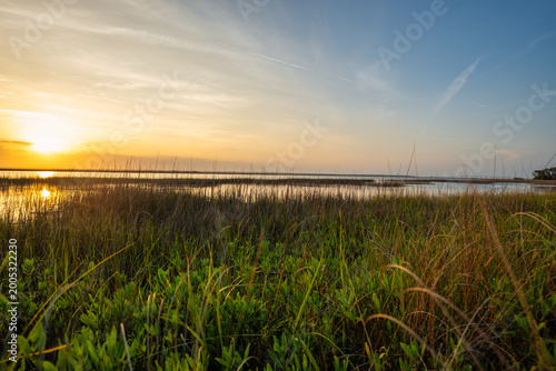 Sunset over a marshy area with grass and calm water reflecting the evening sky near a coastal region