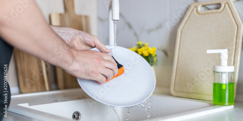 Obraz na plátně Person washing dish under running tap at kitchen sink