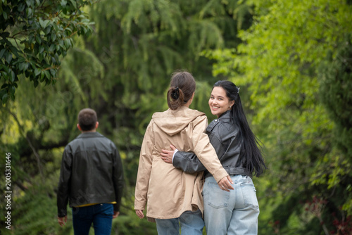 Two women walking arm in arm through a lush green park, smiling together during a peaceful outdoor stroll with friends in nature.