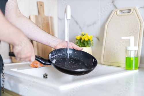 Foto Person rinsing frying pan in kitchen sink with faucet