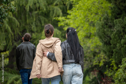 Group of people walking through a lush green park, seen from behind, enjoying a peaceful outdoor stroll in nature.