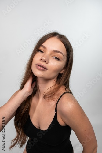 Young woman with natural long hair posing confidently, touching neck, looking at camera in studio