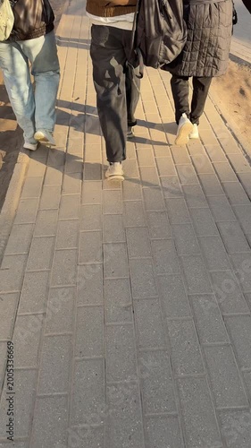 Female students walking footpath campus backpacks spring afternoon sun casting long shadows three friends in jackets and jeans.