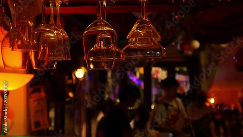 Wine glasses hanging upside down from bar ceiling rack with live music band performing in bokeh background at night