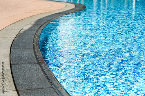 Curved edge of swimming pool with clear blue water and stone border