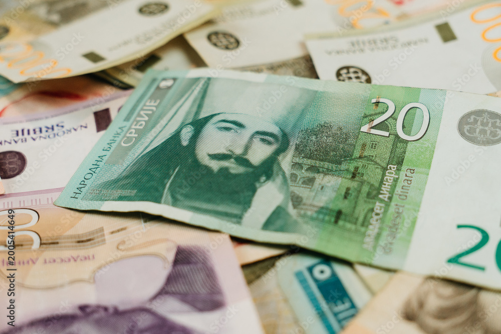 Obraz premium A twenty Serbian dinar banknote lies over scattered Serbian cash on the table. Small denomination currency concept for local payment, retail pricing and everyday spending