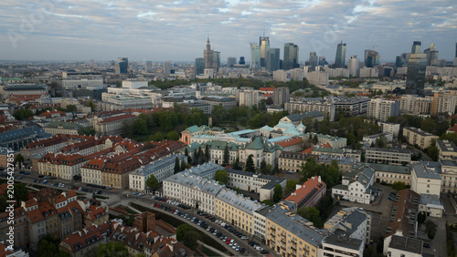 Aerial view from Warsaw's Old Town: intimate view of terracotta rooftops and spires, gazing toward distant Palace of Culture piercing the skyline, no river in frame